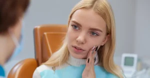 Young woman experiencing tooth pain during a dental consultation, symbolizing urgent and non-urgent dental emergencies.